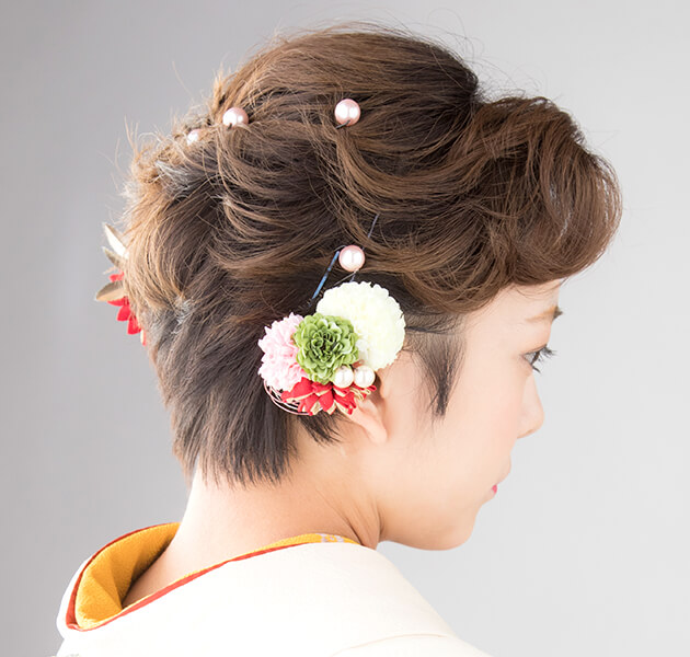 髪の毛をねじって動きを出し両サイドに花飾りを付けたショートヘアーのモデルの横顔写真