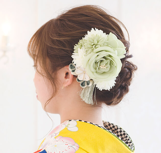 薄緑の花飾りと細かい編み込みシニヨンのモデルの左横顔写真