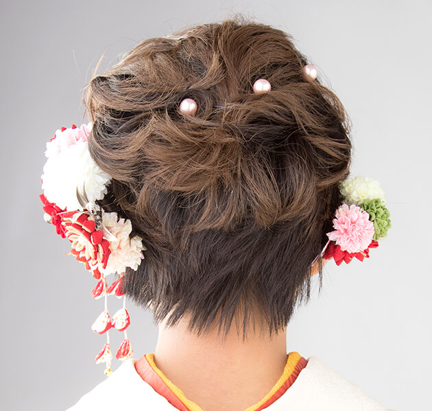 髪の毛をねじって動きを出し両サイドに花飾りを付けたショートヘアーのモデルの後ろ姿写真