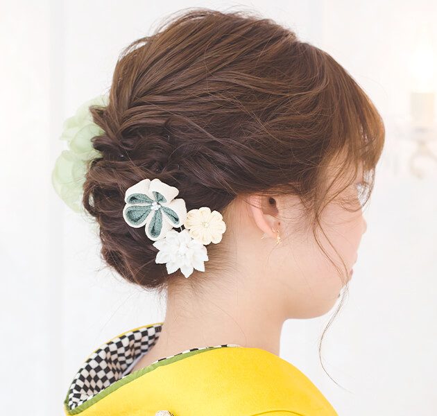 薄緑の花飾りと細かい編み込みシニヨンのモデルの右横顔写真
