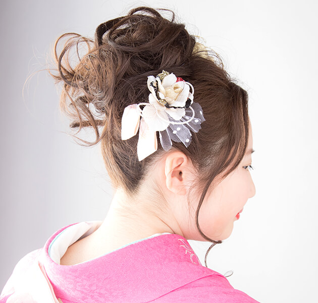 髪を高く盛って白い花飾りを付けたアップスタイルのモデルの右横顔写真