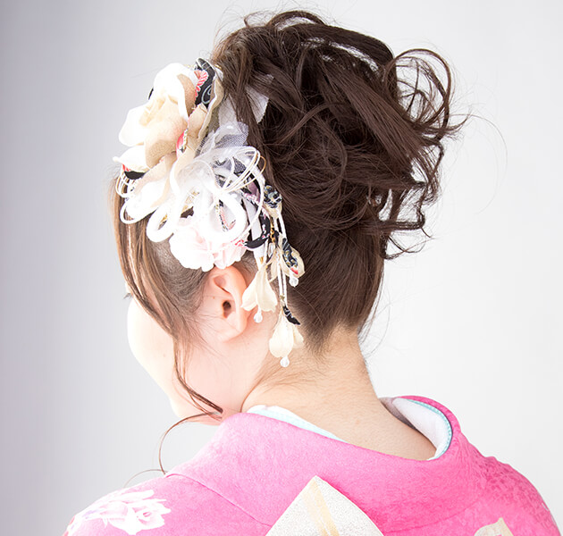 髪を高く盛って白い花飾りを付けたアップスタイルのモデルの左横顔写真
