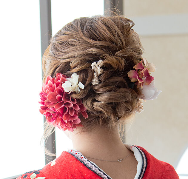 赤の花飾りと低い位置のアップスタイルで大人っぽく髪をまとめたモデルの後ろ姿写真