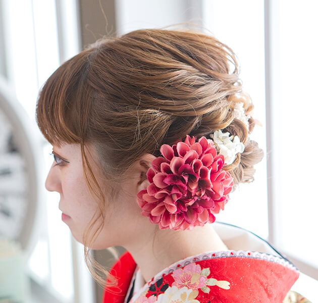 赤の花飾りと低い位置のアップスタイルで大人っぽく髪をまとめたモデルの横顔写真